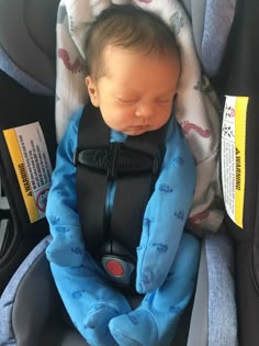 a baby sleeping in a car seat wearing a blue blanket