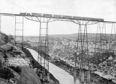 an old black and white photo of a bridge over a river with power lines above it