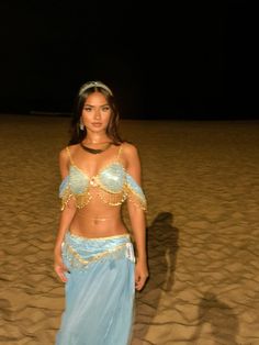 a woman standing on top of a sandy beach wearing a blue belly dance skirt and headpiece