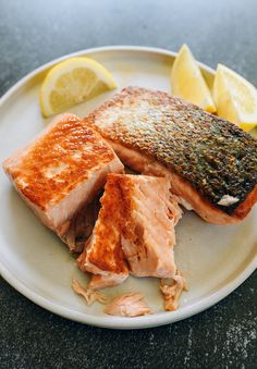 salmon and lemon slices on a white plate with seasoning sprinkled on the side