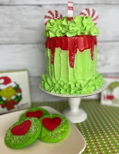 there is a green cake with red hearts on it and two cookies next to it