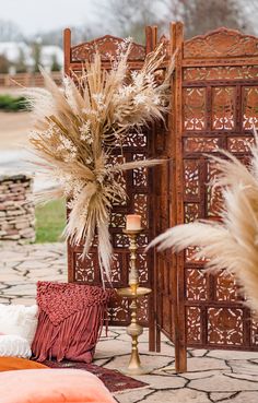 a tall vase filled with dry grass next to a wooden door and decorative wall panel