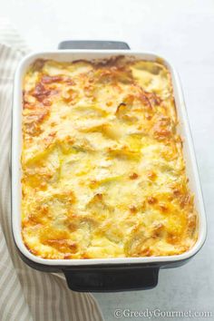 a casserole dish with cheese and vegetables in it on a striped cloth next to a fork