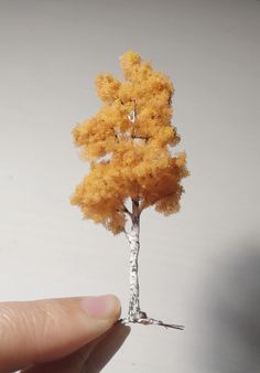 a miniature tree is being held up by someone's hand with yellow leaves on it