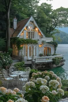 a white house sitting on top of a lush green hillside next to a lake filled with lots of flowers