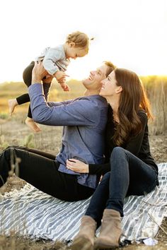 a woman holding a baby while sitting on top of a blanket