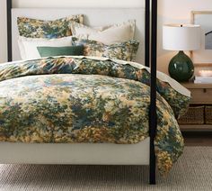 a bed with a floral comforter and pillows on it in front of a night stand