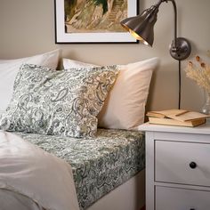 a bed with white sheets and pillows next to a lamp