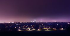 the city skyline is lit up at night with lights in the foreground and fog in the background