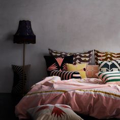 a bed with many pillows on it and a lamp in the corner next to it