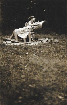 an old black and white photo of a woman laying on a blanket in the grass