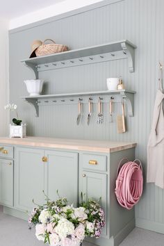 a kitchen with green cabinets and pink flowers on the counter top, hanging utensils