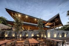 an outdoor dining area with wooden tables and chairs next to a stone wall at dusk