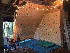 a man is climbing up the side of a wooden structure with lights strung over it