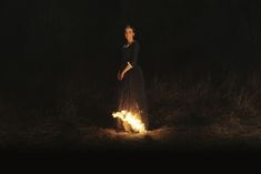 a woman standing in the dark with her hands on her hips and glowing fire behind her