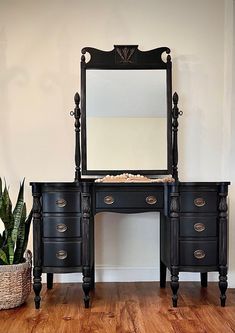 a black dresser with mirror and potted plant in front of it on hard wood flooring