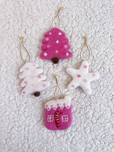 three ornaments are hanging on a white carpet with pink and white decorations in the shape of houses