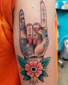 a woman's hand with two fingers and flowers on her left arm, in front of an orange t - shirt