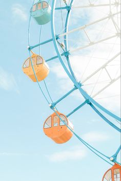 the ferris wheel is orange and blue with two seats on each side, against a bright blue sky