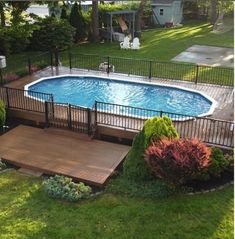 an above ground pool surrounded by lush green grass and trees, next to a deck