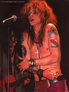 a shirtless man with tattoos on his arm and chest holding a guitar in front of a microphone