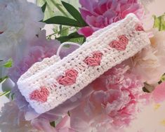 two crocheted headbands with hearts on them sitting next to pink flowers