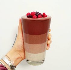 a person holding up a chocolate dessert with raspberries on top in front of a white wall