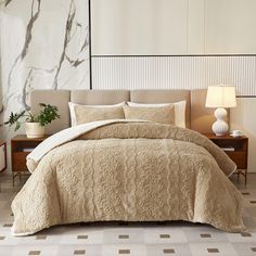 a bed with a beige comforter and two lamps on nightstands in front of a marble wall