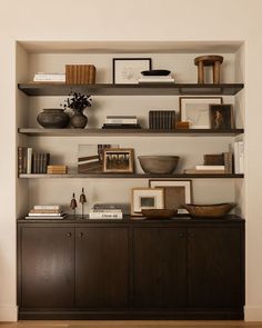 a shelf with books, pictures and other items on it in a living room area