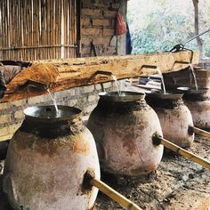 three large pots with water running from them in front of a brick wall and wooden beams