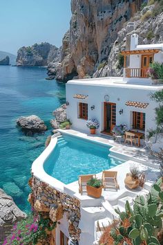 an outdoor swimming pool next to the ocean with chairs and tables around it, surrounded by greenery