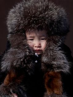 a young child wearing a fur coat and hood, looking at the camera with an intense look on his face