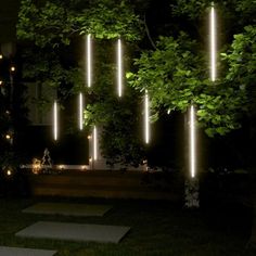 some lights that are hanging from the side of a building in the dark, with trees and grass