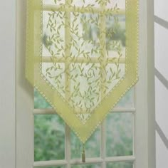 a window with a yellow lace curtain hanging from it's side, in front of a white wall