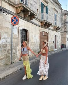 two women walking down the street holding hands with each other in front of an old building