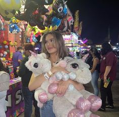 a woman holding two stuffed animals in her arms at an amusement park with other people