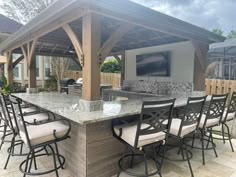 an outdoor kitchen with bar seating and television on the back wall, surrounded by patio furniture