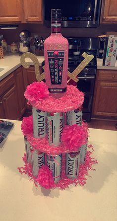 a birthday cake made to look like a vodka bottle with pink feathers and gold letters