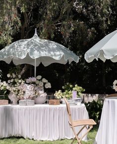 an outdoor table with two umbrellas over it and flowers in vases on the table