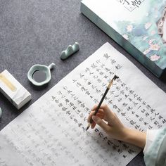 a woman is writing on paper with chinese characters and other items around her, including an ink pen