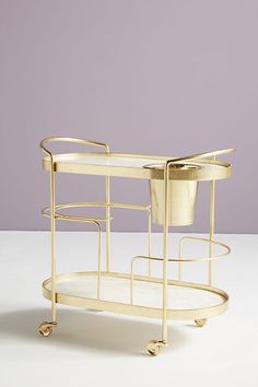 a gold serving cart with two trays and a flower pot on the bottom shelf