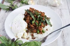 a white plate topped with rice and meat next to a green leafy plant on a table