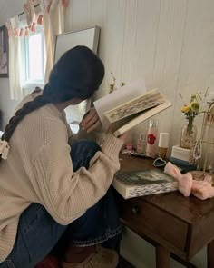 a woman sitting at a desk with an open book in front of her and looking through the pages