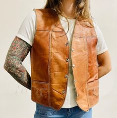 A great staple piece for any wardrobe! This unisex vest is made from Genuine leather with a faux Sherpa lining made from what I believe to be acrylic pile, although actual material of lining is not listed on any tags. The vest has metal snap buttons, 2 front pockets, and features beautiful stitching detail. The vest was made in Mexico and has no major flaws to note.  Best fits a Women's M/L Shoulder to shoulder: 14.5" Pit to Pit: 18.5" Length: 23" My sizing is an estimate of general modern day sizing and vintage sizes vary and are different from current, I modern day sizing. Please see measurements above to get the most accurate sense of fit.  Measurements are taken with the garment lying flat, so please double the measurements where appropriate (waist, hips, etc). Model is 5' 3". Wears a Western Vest, Western Shop, Have Metal, Vest Outfits, Sherpa Lined, Staple Pieces, Vintage 1970s, Snap Button, Genuine Leather