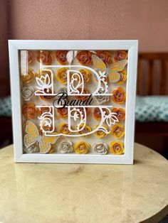 a white frame with flowers and the word b is displayed on a table in front of a chair