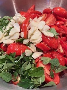 a metal bowl filled with lots of tomatoes and green leafy vegetables on top of it