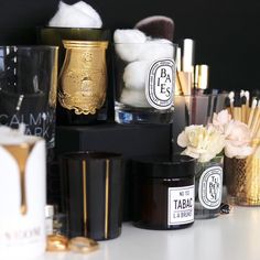 several different types of makeup brushes and containers on a white table with flowers in vases