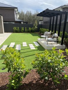 a backyard with artificial grass and seating area in the middle, surrounded by shrubbery