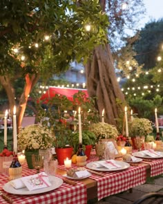 a table set for dinner with candles and flowers in the center, surrounded by greenery