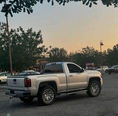 a silver truck parked in a parking lot next to other cars and trees at sunset